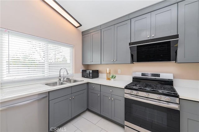 kitchen with vaulted ceiling, gray cabinets, sink, stainless steel range with gas cooktop, and light tile patterned floors