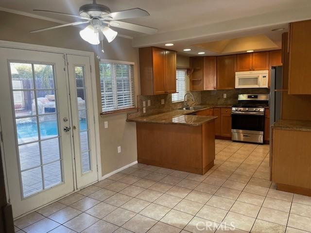 kitchen featuring sink, backsplash, stainless steel gas range oven, light tile patterned flooring, and kitchen peninsula