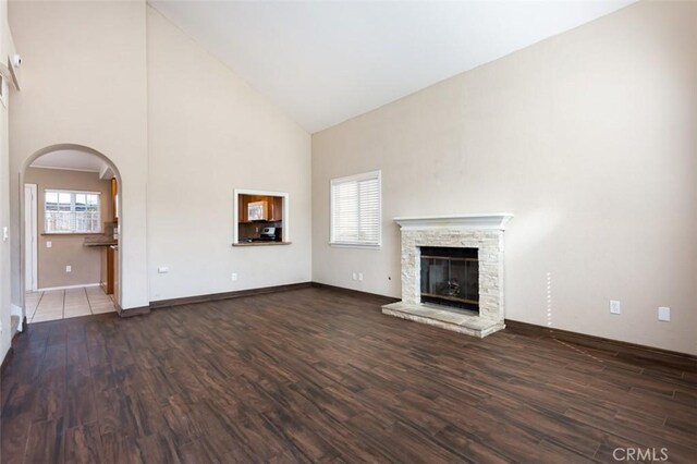 unfurnished living room featuring dark hardwood / wood-style flooring, a stone fireplace, and high vaulted ceiling