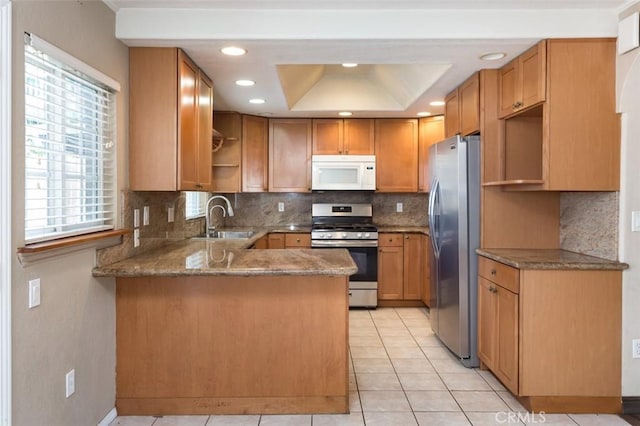 kitchen with sink, appliances with stainless steel finishes, a raised ceiling, light tile patterned flooring, and kitchen peninsula