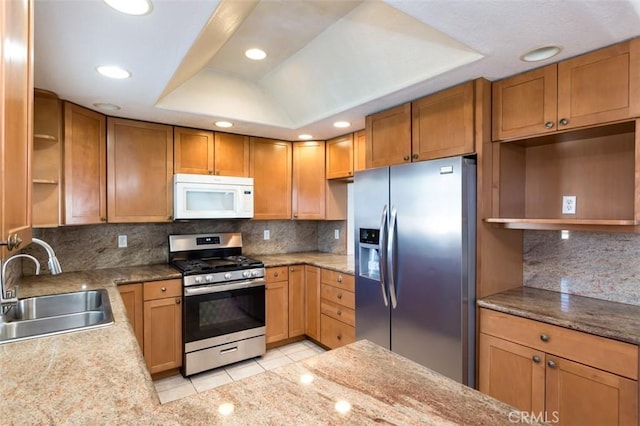 kitchen featuring sink, backsplash, stainless steel appliances, a tray ceiling, and light tile patterned flooring