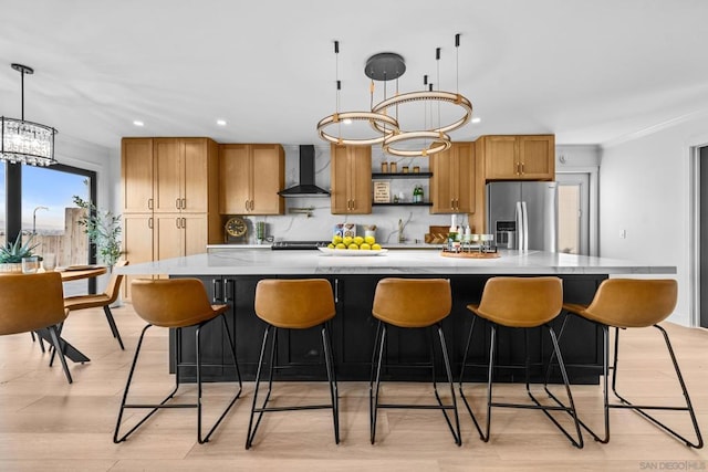 kitchen with a spacious island, wall chimney exhaust hood, stainless steel refrigerator with ice dispenser, an inviting chandelier, and hanging light fixtures