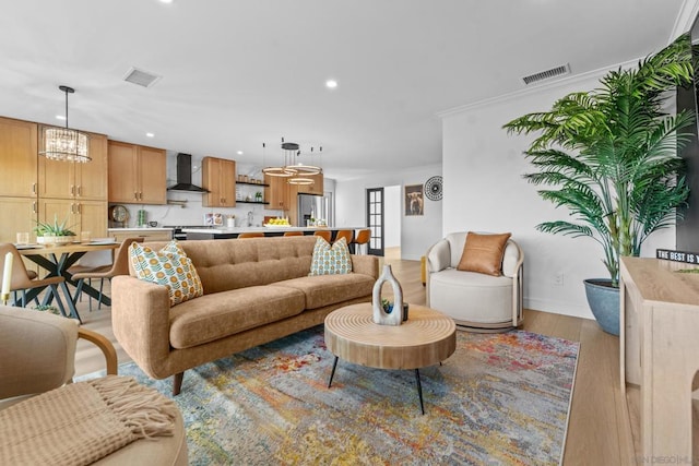 living room featuring a notable chandelier, ornamental molding, and light hardwood / wood-style floors