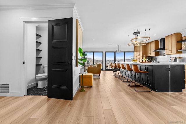 interior space with pendant lighting, kitchen peninsula, a kitchen breakfast bar, ornamental molding, and wall chimney exhaust hood