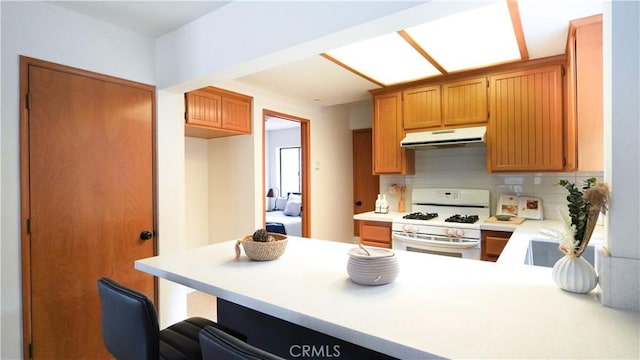 kitchen with white gas stove, backsplash, and kitchen peninsula