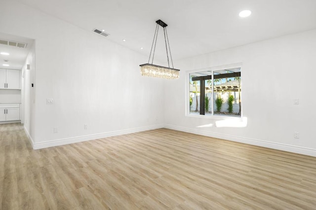 unfurnished room featuring an inviting chandelier and light hardwood / wood-style flooring