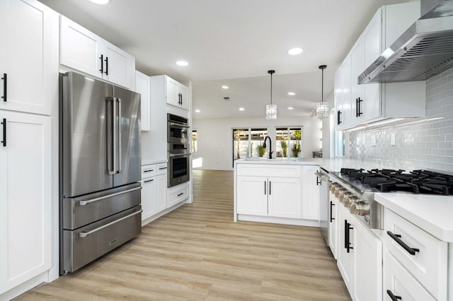 kitchen with appliances with stainless steel finishes, decorative light fixtures, white cabinetry, wall chimney range hood, and kitchen peninsula