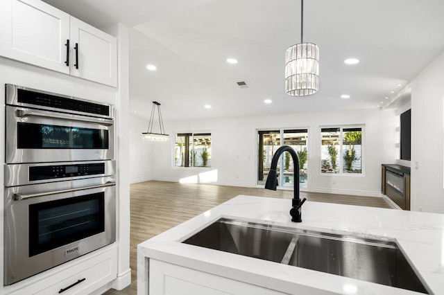 kitchen featuring decorative light fixtures, sink, white cabinetry, stainless steel double oven, and light stone counters