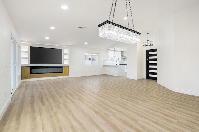 unfurnished living room with sink, a notable chandelier, and light wood-type flooring