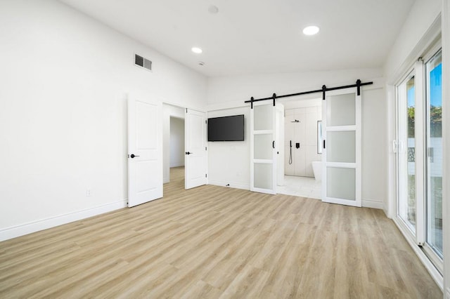 unfurnished bedroom with light hardwood / wood-style flooring, access to outside, a barn door, and vaulted ceiling