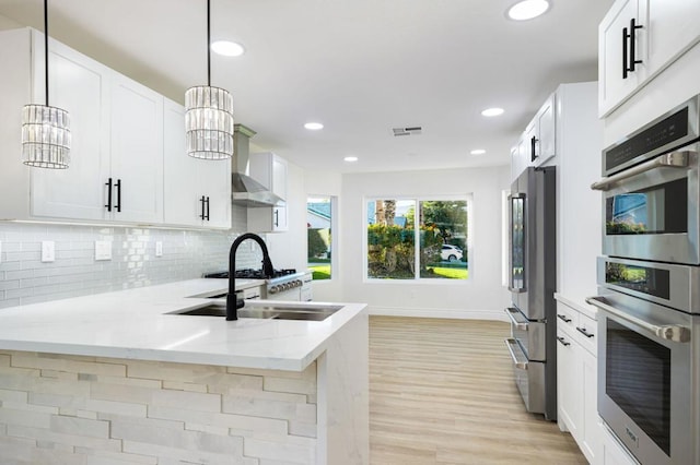 kitchen featuring white cabinets, appliances with stainless steel finishes, an inviting chandelier, hanging light fixtures, and light stone counters