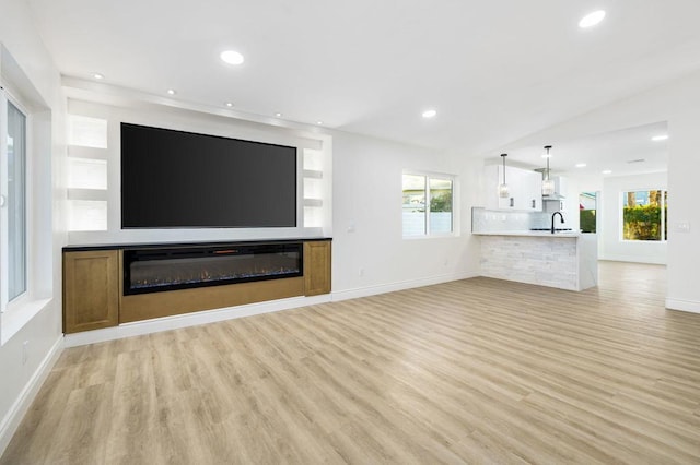 unfurnished living room featuring lofted ceiling, light hardwood / wood-style flooring, and sink