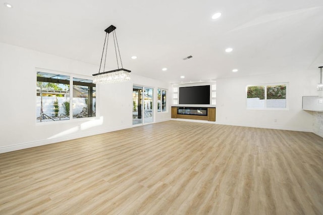 unfurnished living room with plenty of natural light, light hardwood / wood-style flooring, and an inviting chandelier