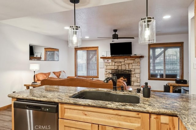 kitchen featuring ceiling fan, dishwasher, pendant lighting, sink, and a stone fireplace