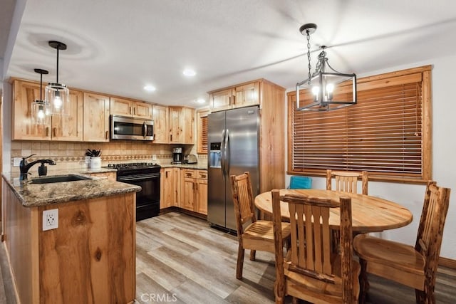 kitchen with decorative light fixtures, kitchen peninsula, sink, stainless steel appliances, and dark stone counters