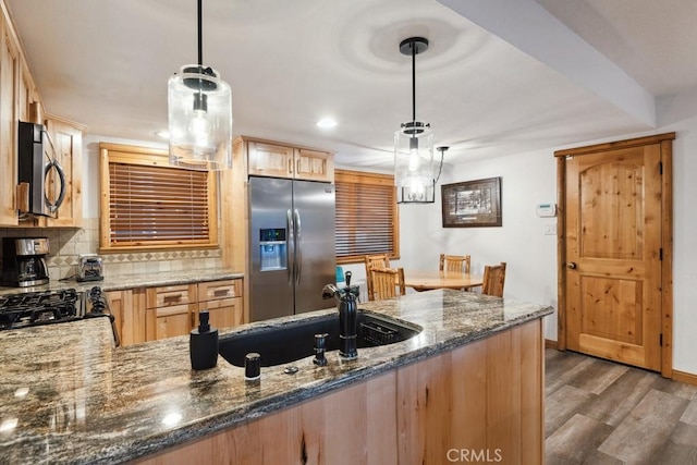 kitchen featuring kitchen peninsula, appliances with stainless steel finishes, backsplash, decorative light fixtures, and dark stone countertops