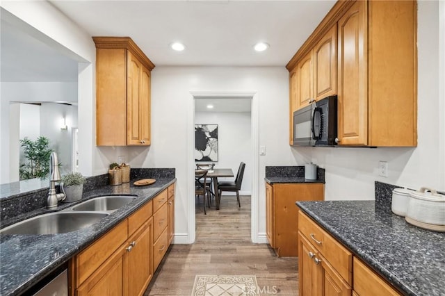 kitchen featuring light wood-style flooring, a sink, dark stone countertops, black microwave, and dishwasher