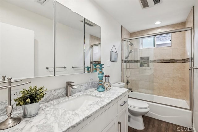 bathroom with bath / shower combo with glass door, visible vents, toilet, vanity, and wood finished floors