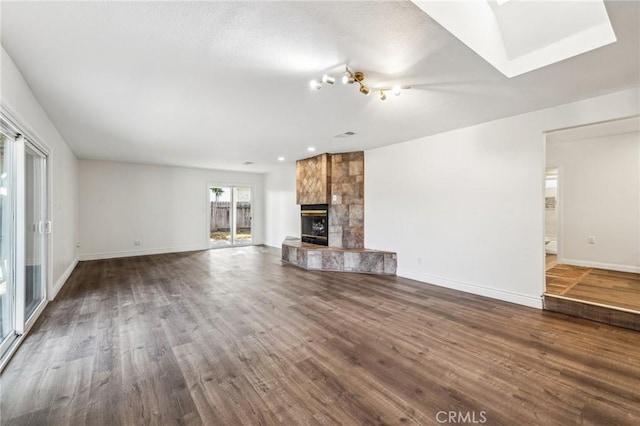 unfurnished living room featuring dark wood-style floors, a tile fireplace, and baseboards