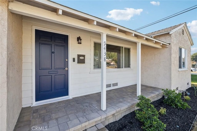 view of exterior entry with a porch and stucco siding