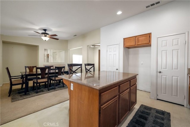 kitchen featuring ceiling fan, a kitchen island, and light stone countertops