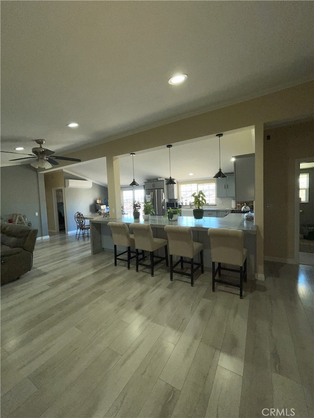 kitchen featuring hanging light fixtures, stainless steel refrigerator, light wood-type flooring, ceiling fan, and a breakfast bar