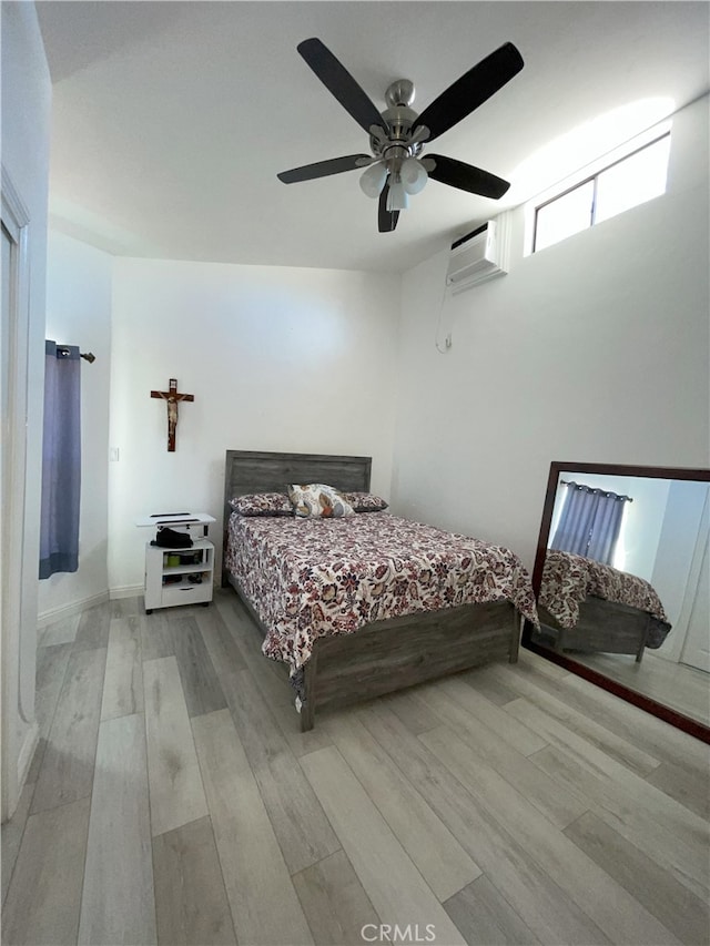 bedroom with ceiling fan, an AC wall unit, and light wood-type flooring