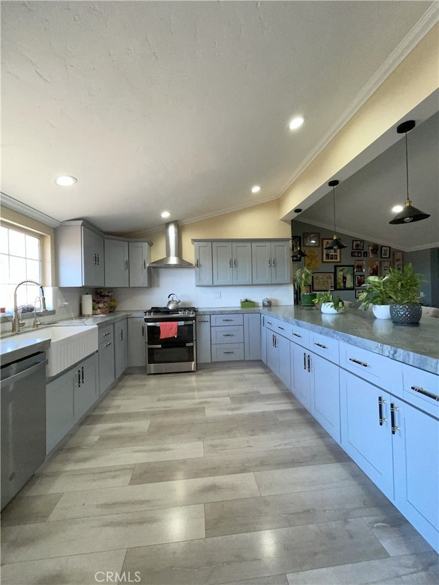 kitchen with pendant lighting, lofted ceiling, wall chimney range hood, stainless steel appliances, and sink