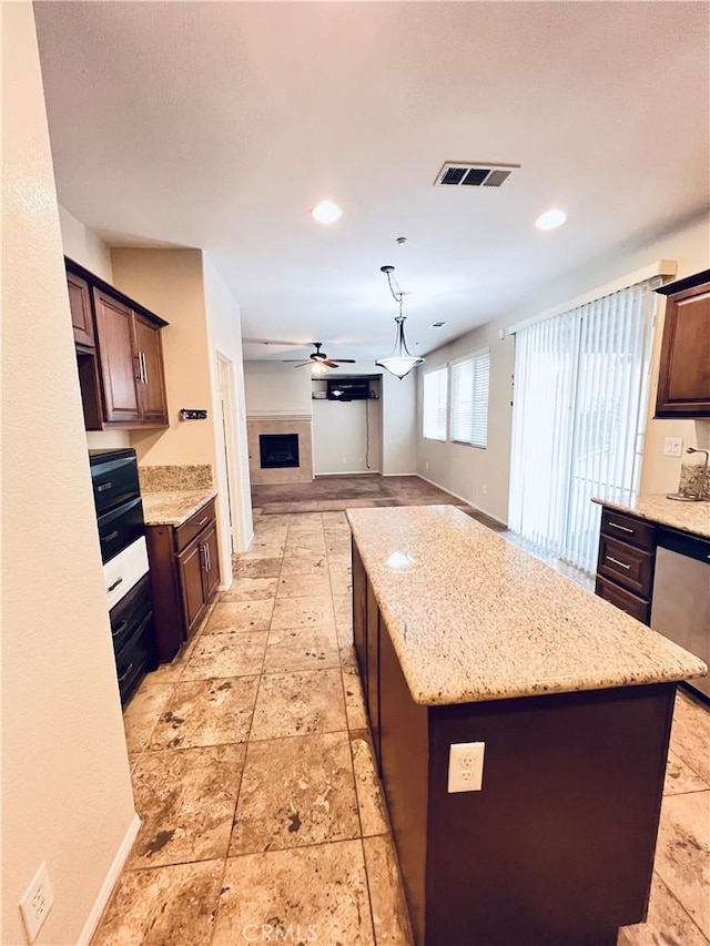 kitchen with ceiling fan, dishwasher, a center island, dark brown cabinetry, and light stone counters