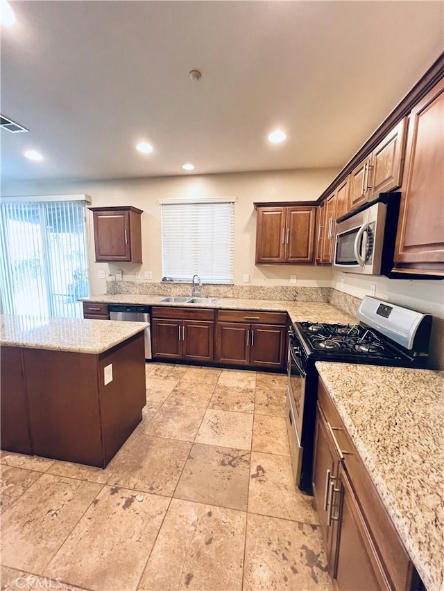 kitchen featuring appliances with stainless steel finishes, light stone counters, dark brown cabinetry, and sink