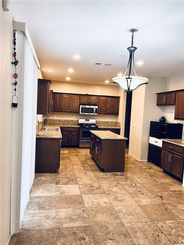 kitchen featuring appliances with stainless steel finishes, a kitchen island, sink, hanging light fixtures, and dark brown cabinets