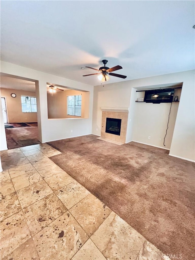 unfurnished living room with ceiling fan, plenty of natural light, carpet, and a tile fireplace