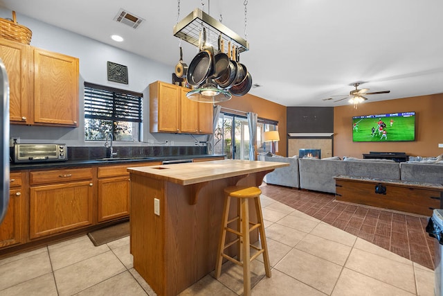 kitchen featuring wooden counters, a center island, sink, light tile patterned flooring, and a tiled fireplace