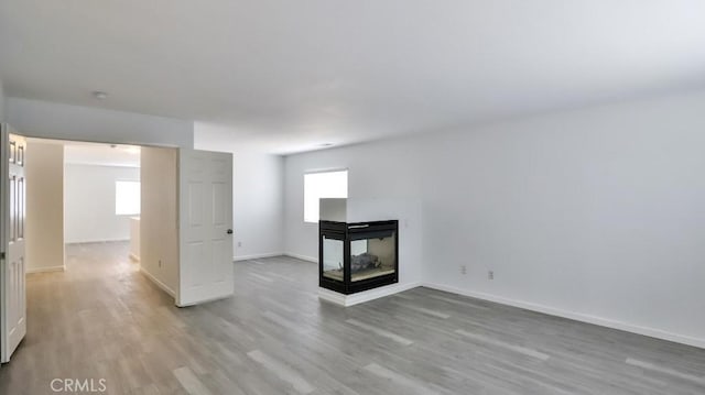 unfurnished living room with a multi sided fireplace and light hardwood / wood-style floors