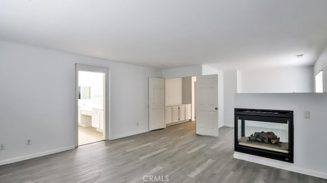 unfurnished living room featuring a multi sided fireplace and light hardwood / wood-style floors