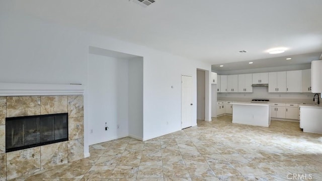 kitchen with a fireplace, sink, white cabinetry, and a kitchen island