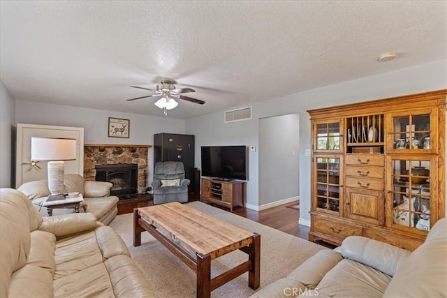 living room featuring a textured ceiling, ceiling fan, a fireplace, and wood-type flooring