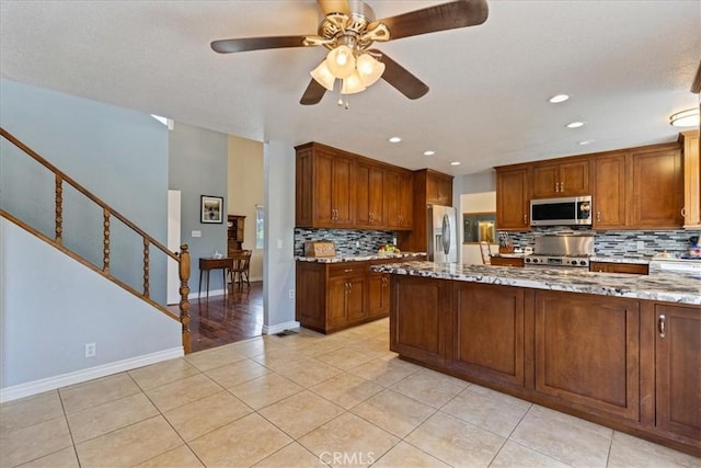 kitchen featuring light tile patterned floors, ceiling fan, stainless steel appliances, decorative backsplash, and light stone counters