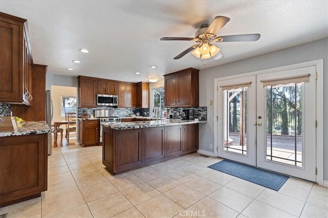 kitchen featuring kitchen peninsula, ceiling fan, stainless steel appliances, french doors, and light stone countertops