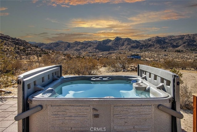 pool at dusk with a mountain view and a hot tub