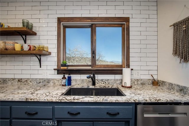 kitchen with stainless steel dishwasher, blue cabinetry, light stone counters, and sink