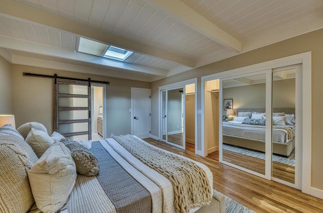 bedroom with a skylight, a barn door, wooden ceiling, light wood-type flooring, and beam ceiling