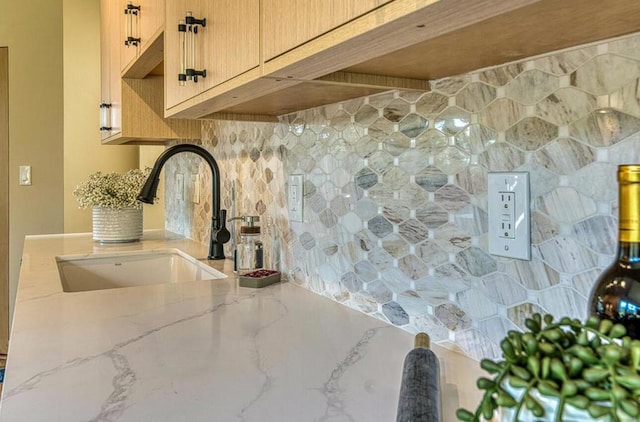 kitchen featuring light stone counters, sink, light brown cabinets, and backsplash