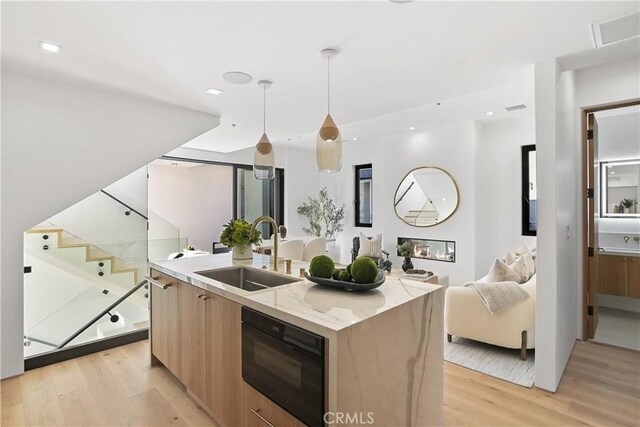 kitchen featuring light stone countertops, sink, hanging light fixtures, light wood-type flooring, and a center island with sink