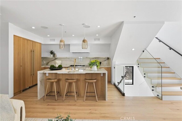 kitchen featuring pendant lighting, light hardwood / wood-style floors, backsplash, a kitchen island with sink, and a breakfast bar