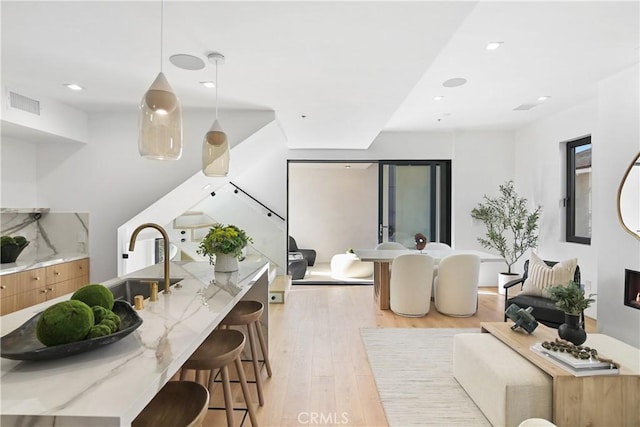 interior space with a breakfast bar area, decorative light fixtures, light wood-type flooring, light stone counters, and sink