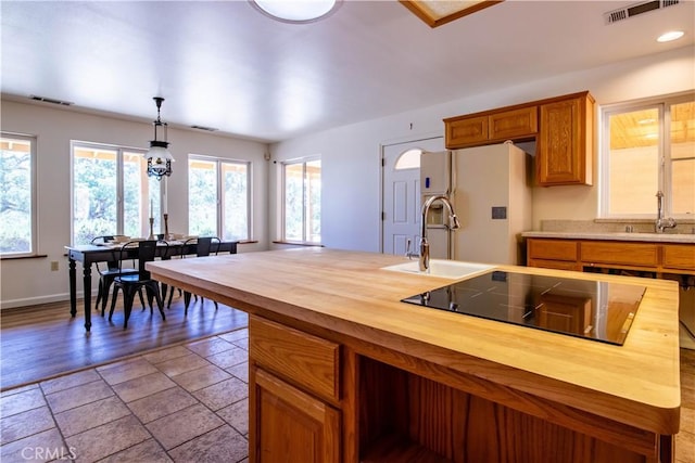 kitchen featuring wood counters, black electric stovetop, white fridge with ice dispenser, hanging light fixtures, and sink