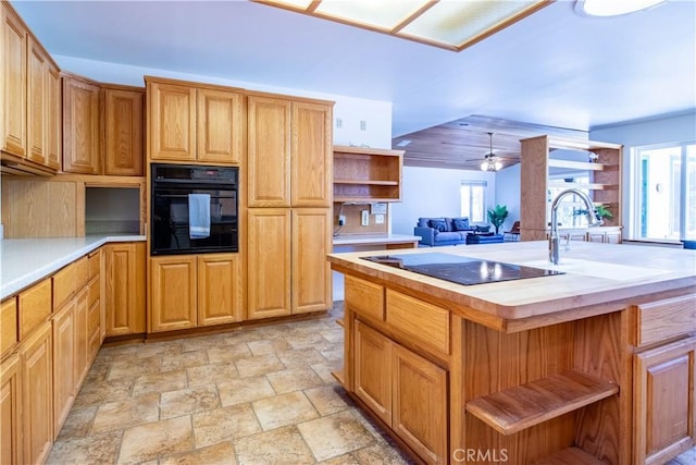 kitchen with ceiling fan, a wealth of natural light, an island with sink, and black appliances