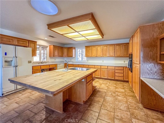 kitchen with black appliances, sink, an island with sink, a breakfast bar area, and butcher block counters