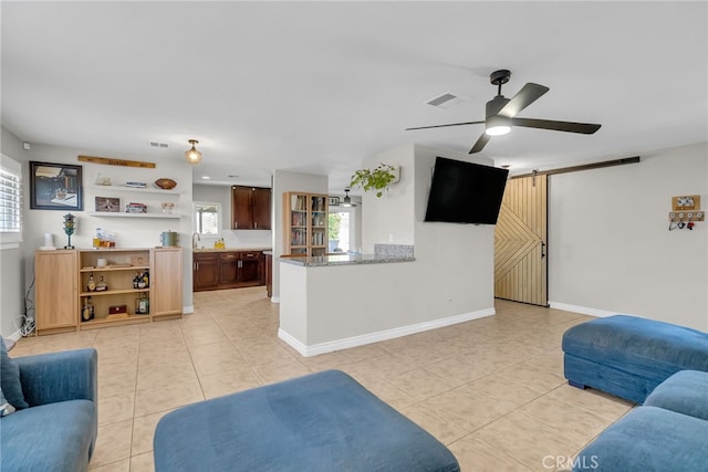 living room with ceiling fan, sink, light tile patterned floors, and a barn door